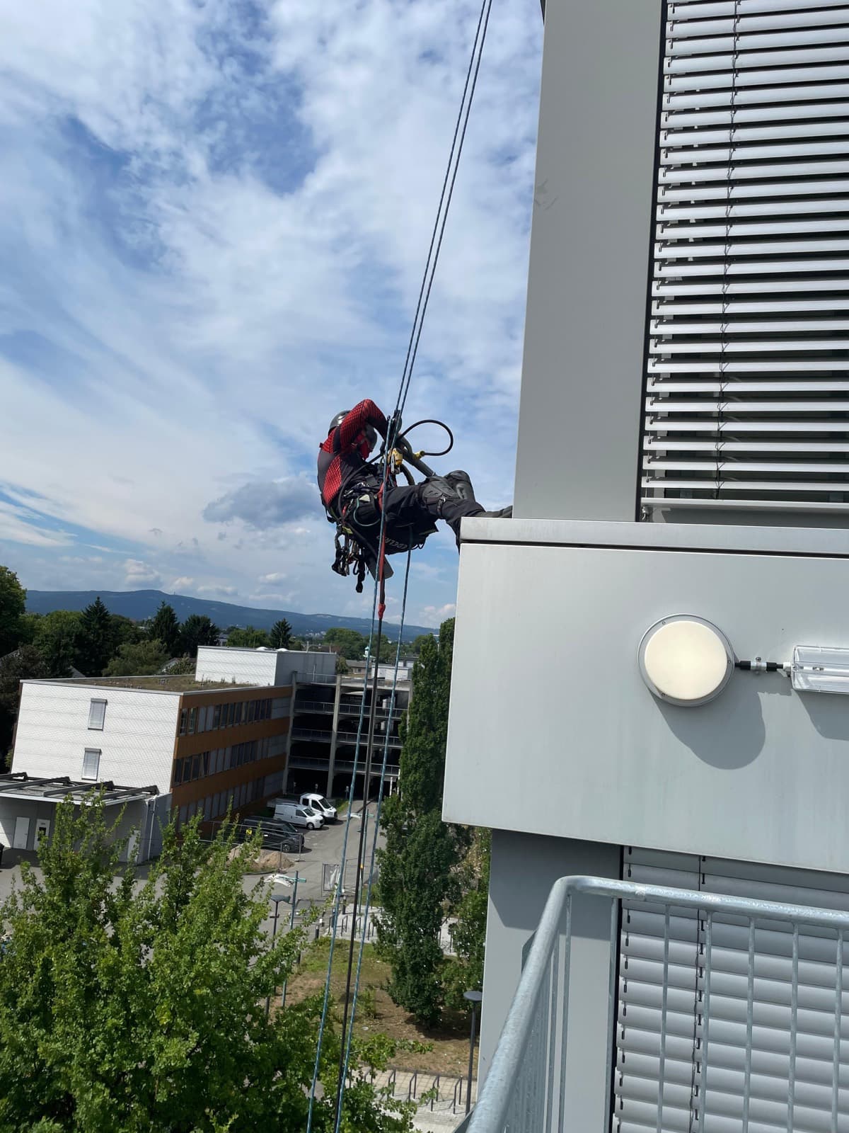Industriekletterer im Seilzugang an einer Gebäudekante vor blauem Himmel